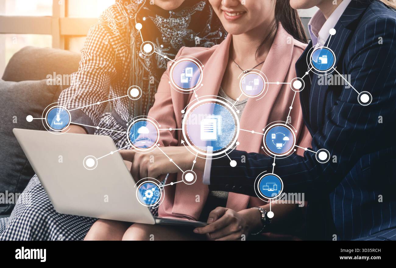 Tre professionisti collaborano su un notebook, interagendo con icone digitali che simboleggiano il networking e il lavoro di squadra, creando un ufficio innovativo Foto Stock