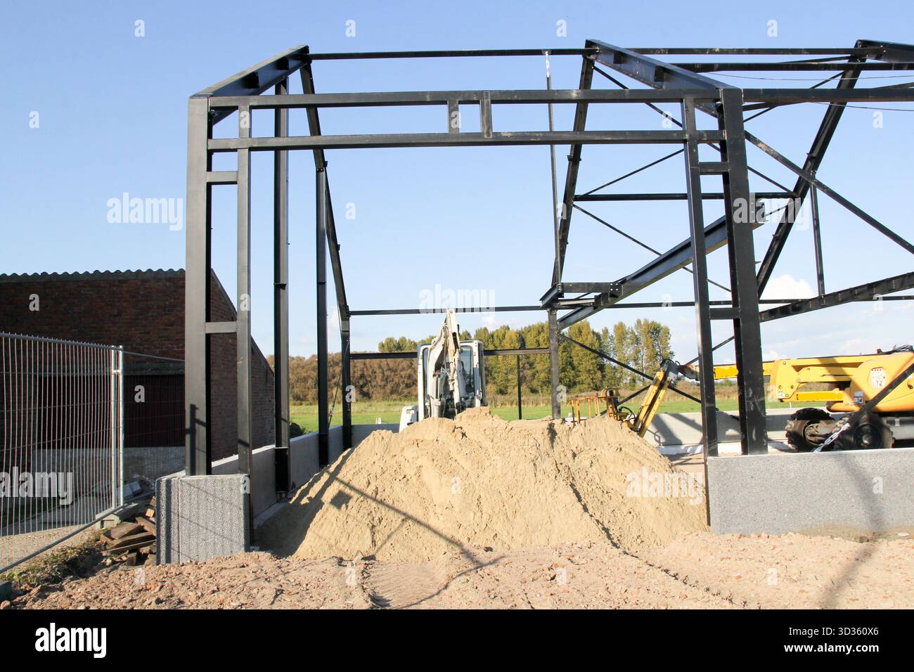 la costruzione in acciaio di un capannone in costruzione e cumuli di sabbia ed escavatori in campagna Foto Stock