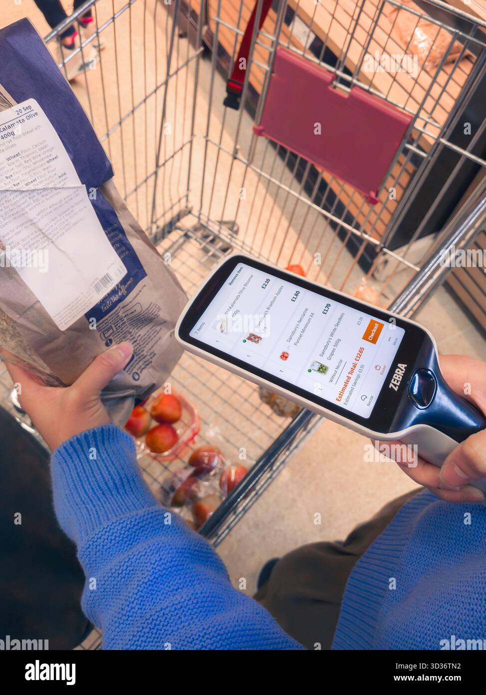 Donna che utilizza uno scanner per la scansione del codice a barre del prodotto per il check-out automatico al supermercato Sainsbury, noto anche come Scan & Go, smartshop & self-checkout, Regno Unito Foto Stock