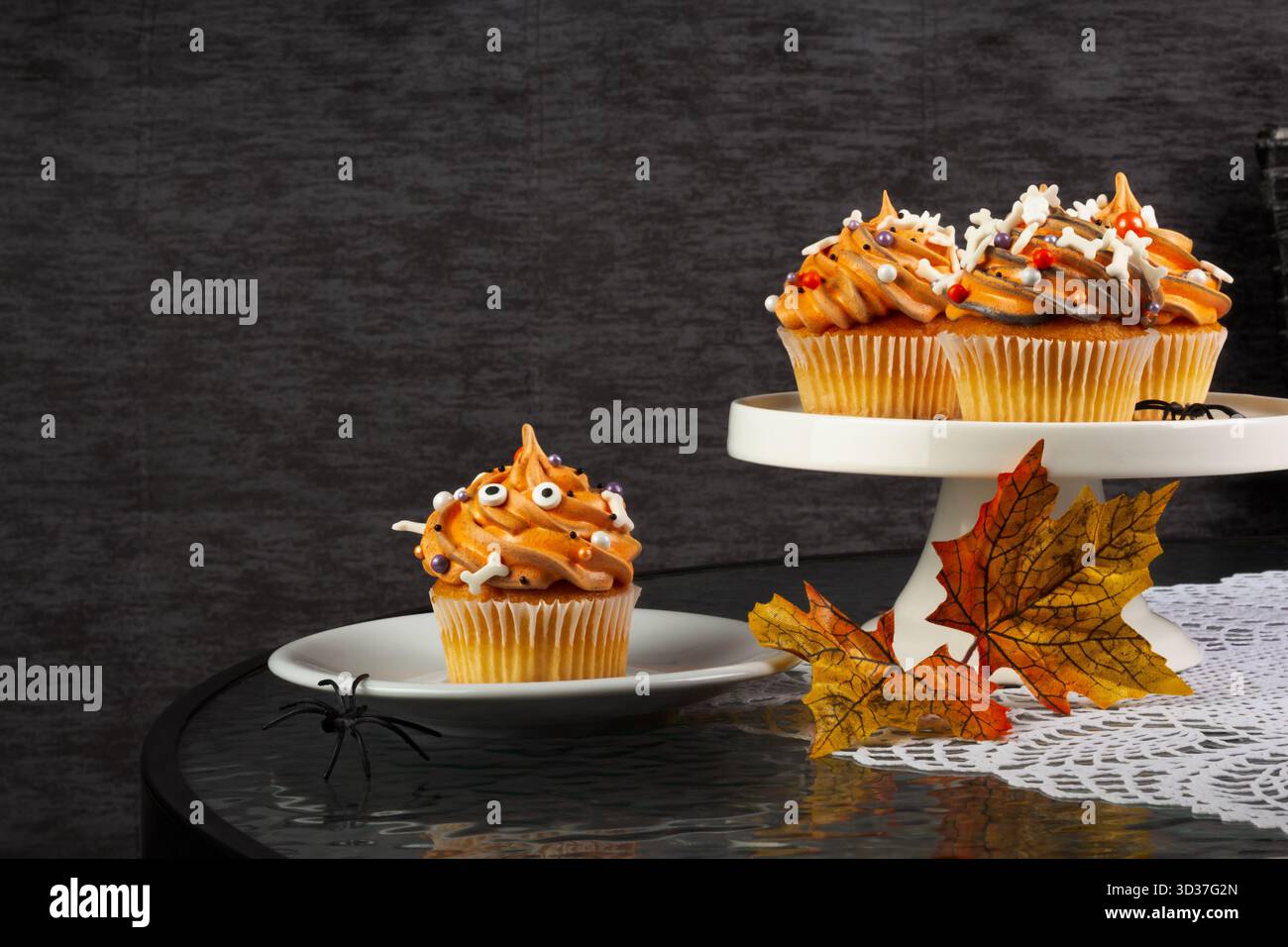 I cupcake con glassa d'arancia e decorazioni giocose sono disposti su un tavolo. Un piccolo piatto presenta un cupcake, mentre un piedistallo ne contiene altri due. Foto Stock
