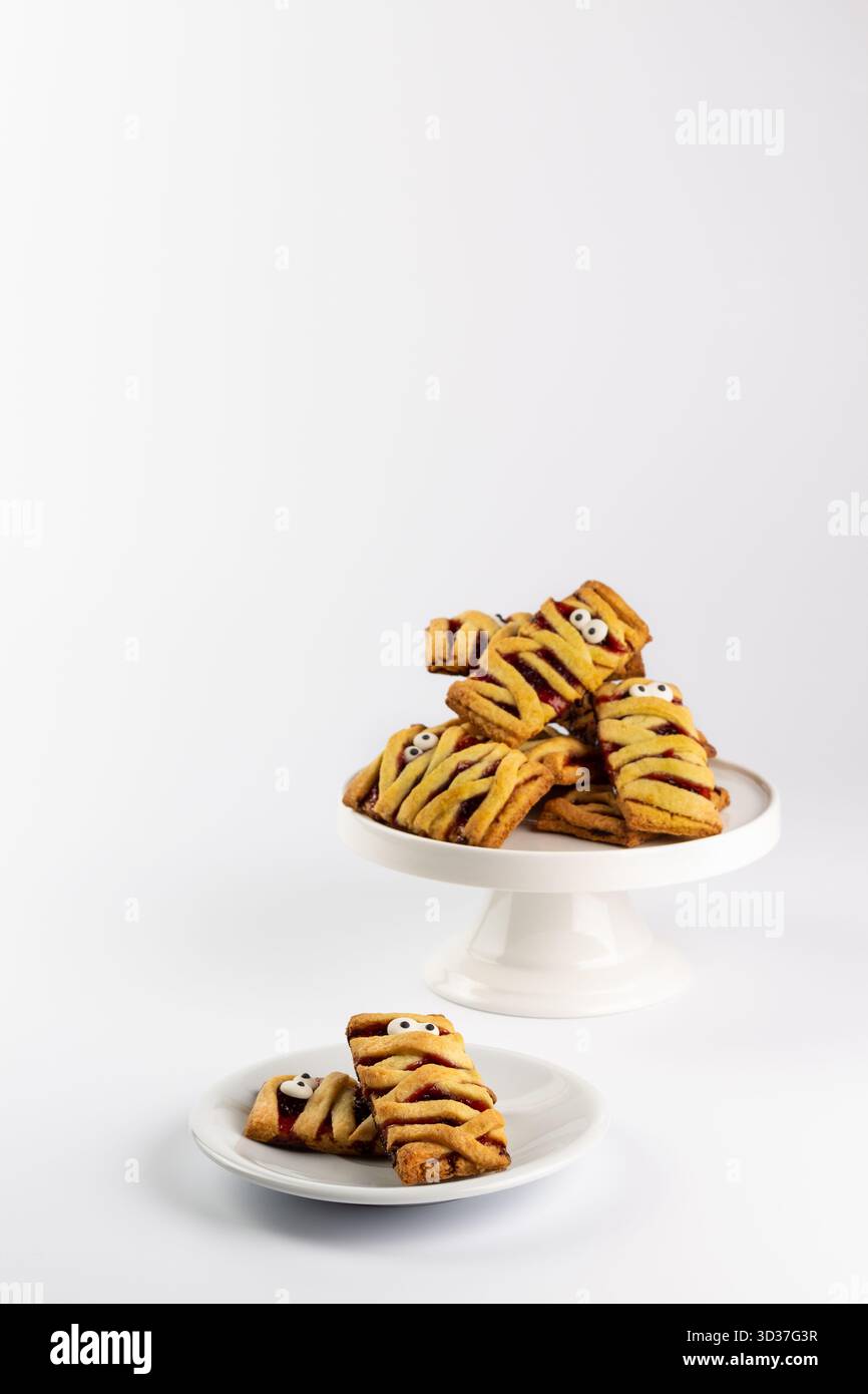 I dolci festivi a forma di mummia si trovano su banchi per torte bianchi, che mostrano i loro intricati disegni. Perfetti per riunioni o celebrazioni di Halloween, questi tr Foto Stock