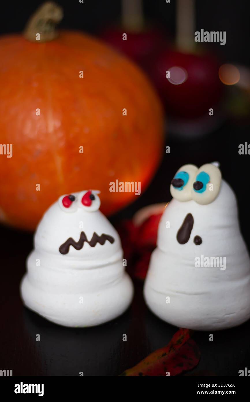 Adorabili spuntini a forma di fantasma con decorazioni colorate sono posizionati vicino a una zucca arancione, creando un'atmosfera festosa e giocosa per Halloween Foto Stock