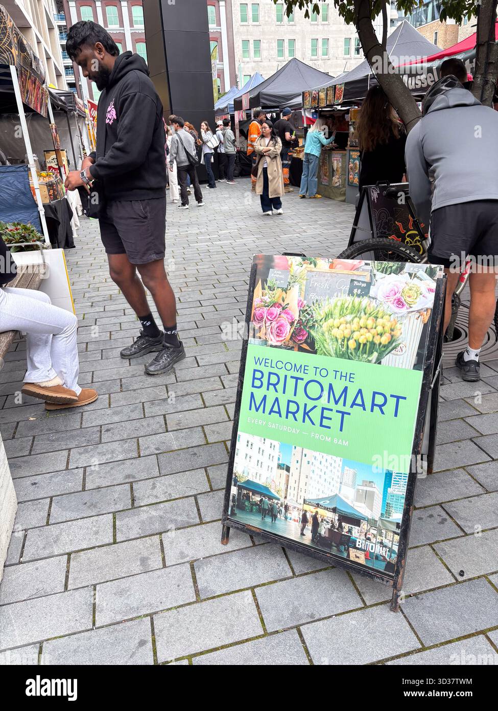 Britomart Market, un mercato agricolo all'aperto di Auckland, nuova Zelanda, con gente che curiosa tra le bancarelle e un importante cartello di benvenuto. Rappresenta la comunicazione locale Foto Stock