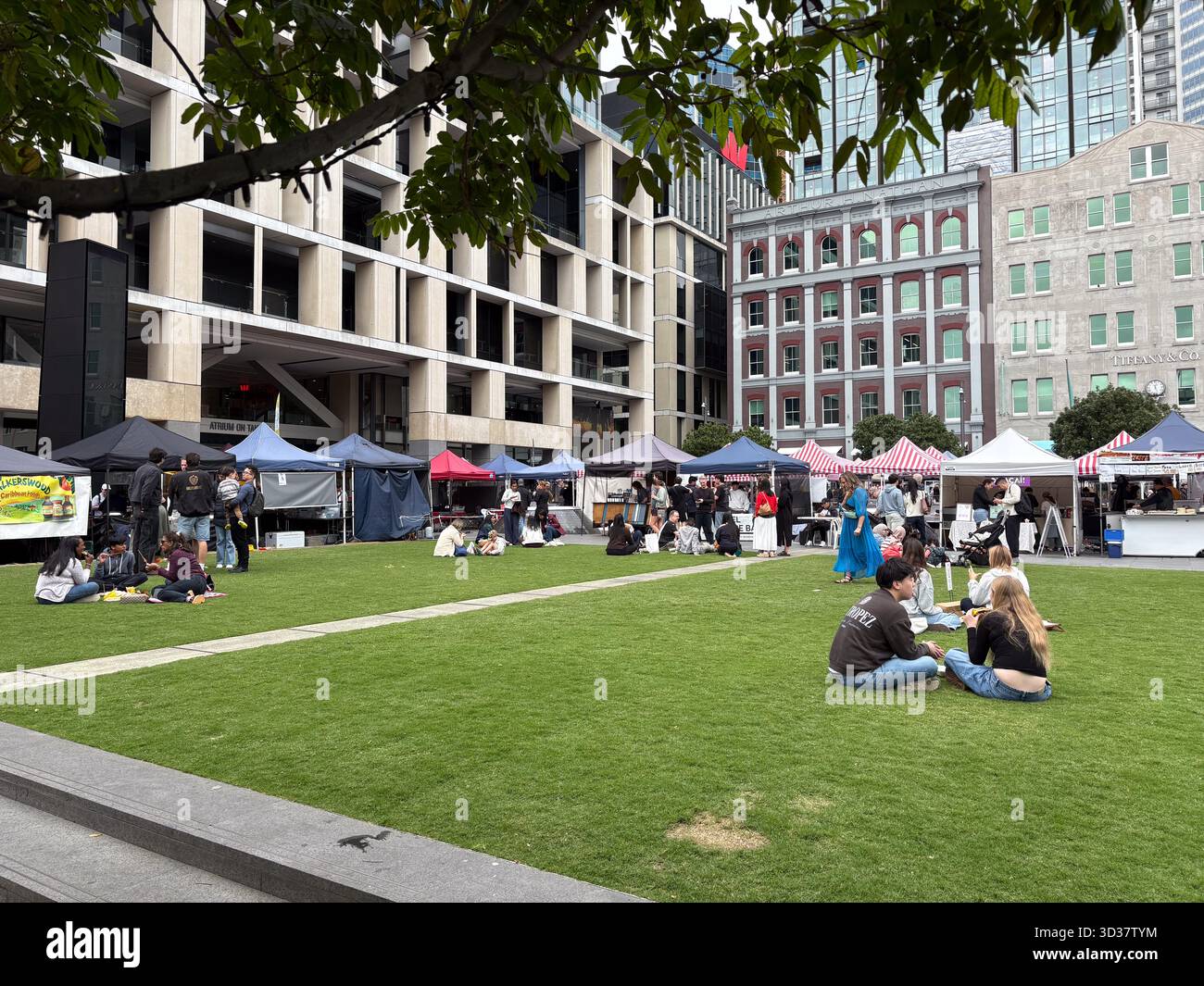 Il Britomart Saturday Market, un vivace mercato agricolo nel centro di Auckland, nuova Zelanda, con gente che si rilassa sull'erba tra bancarelle e bui urbani Foto Stock