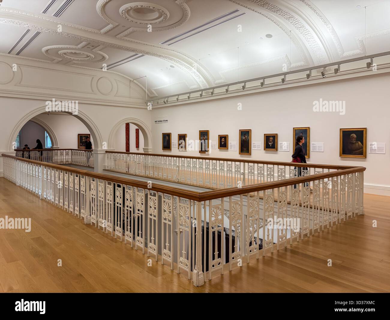 Gli interni della Auckland Art Gallery presentano una luminosa sala con ritratti classici su una parete bianca. Balaustra bianca ornata e corrimano in legno Foto Stock