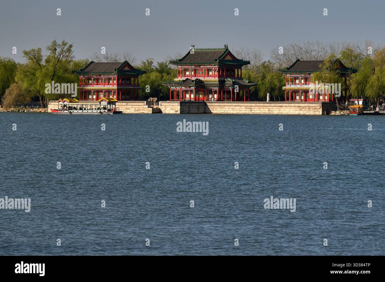 Padiglioni rossi riflessi nell'acqua ferma del lago, composizione orizzontale, riprese alla luce del giorno che catturano l'architettura tradizionale cinese con decorazioni intricate Foto Stock