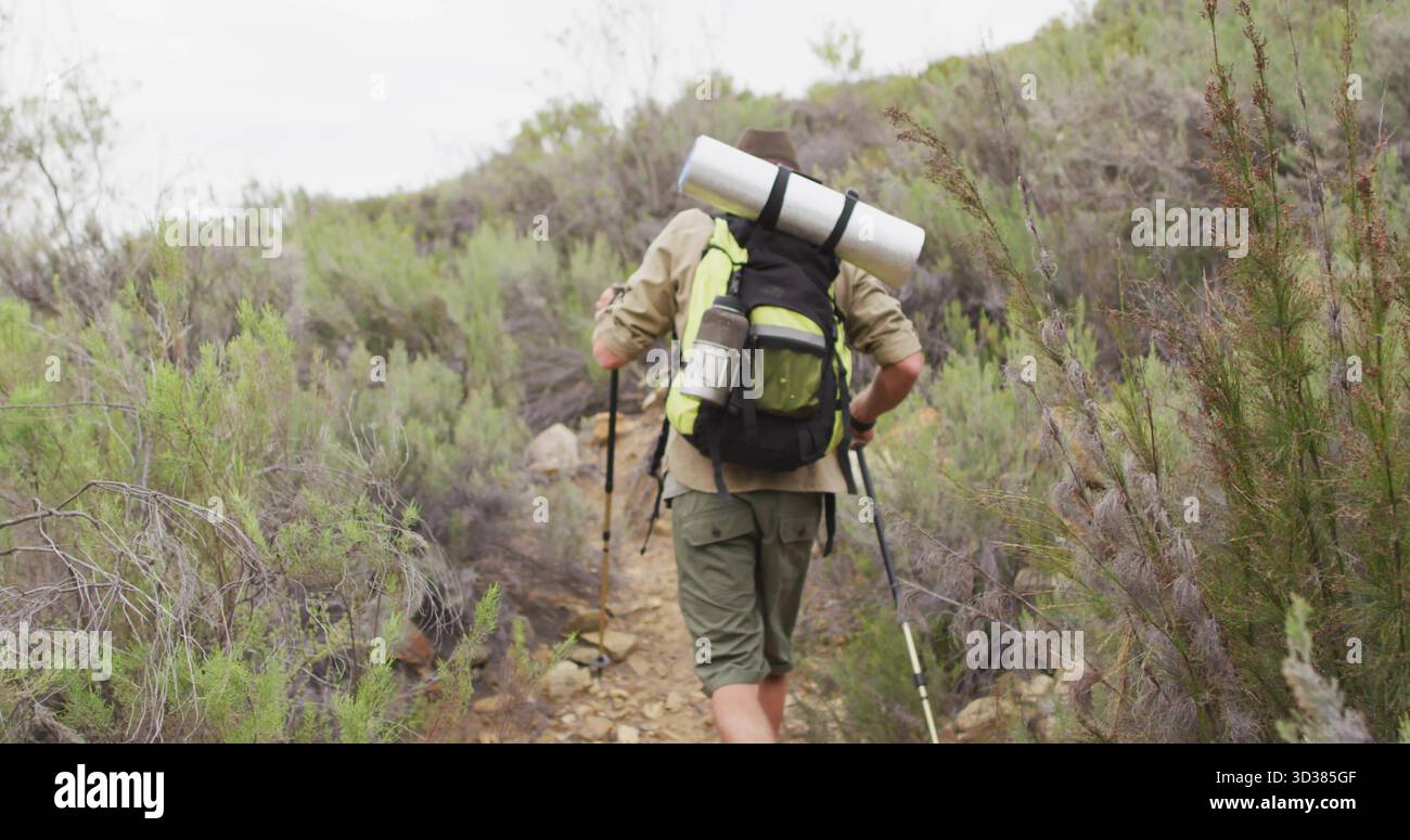 Escursionismo da solo che attraversa il sentiero della macchia rocciosa in salita con zaino carico e bastoncini da trekking Foto Stock