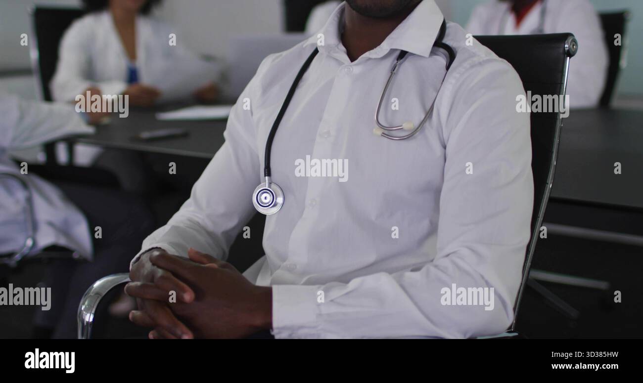 Medico seduto in camicia bianca con stetoscopio che conduce la riunione al tavolo da conferenza con un computer portatile Foto Stock