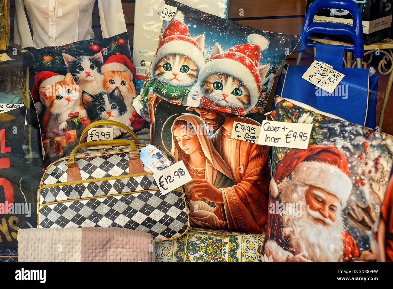 Luminosa vetrina con cuscini decorativi con gattini in cappelli di Natale, Babbo Natale e una scena religiosa. Arredi e accessori accoglienti per le feste Foto Stock