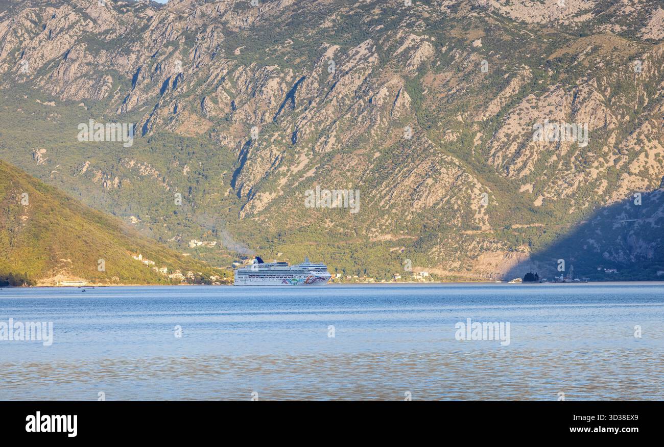 Nave da crociera Norwegian Pearl che entra nella baia di Cattaro, in Montenegro, al mattino presto, con la luce del sole che illumina le montagne e le calme acque blu Foto Stock