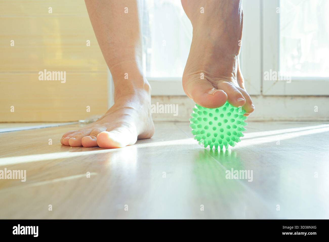 Un piede che fa esercizi con una palla massaggiante sul pavimento a casa. Simboleggia la terapia plantare della fascia, il sollievo dallo stress e la pratica di sensibilizzazione del corpo. Foto Stock