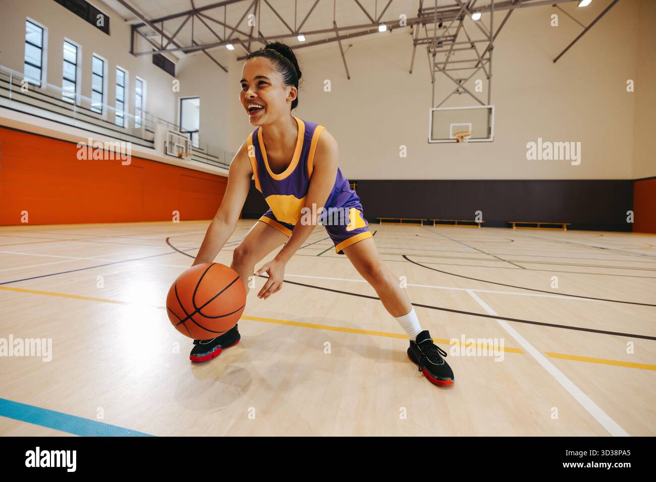 Una giovane atleta vestita di abbigliamento sportivo sorride su un campo da ginnastica. L'immagine mette in risalto fitness, sportività e. Foto Stock