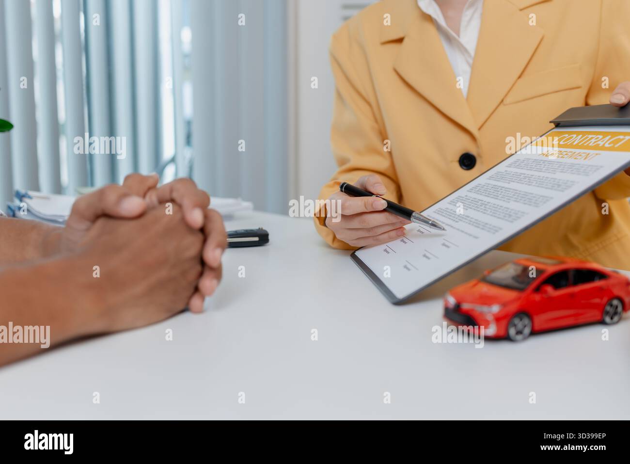 Una negoziazione per la vendita di auto si svolge in un ufficio in cui una donna venditrice con un blazer giallo spiega i dettagli di un contratto a un cliente maschio, showin Foto Stock