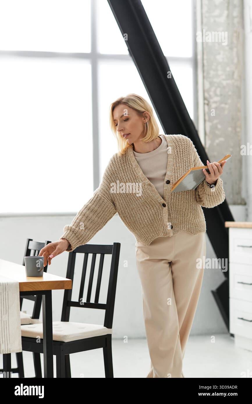 La donna in abbigliamento casual abbraccia il comfort mentre sorseggia il tè nel suo elegante appartamento. Foto Stock