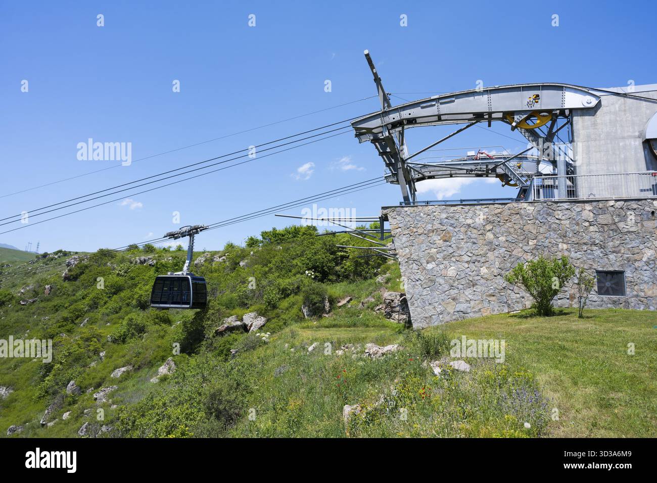 Stazione della funivia con gondola in un paesaggio verde, parete di pietra e cielo blu brillante, funivia Tatev, ali di Tatev, ala Tatev, stazione della funivia, H Foto Stock