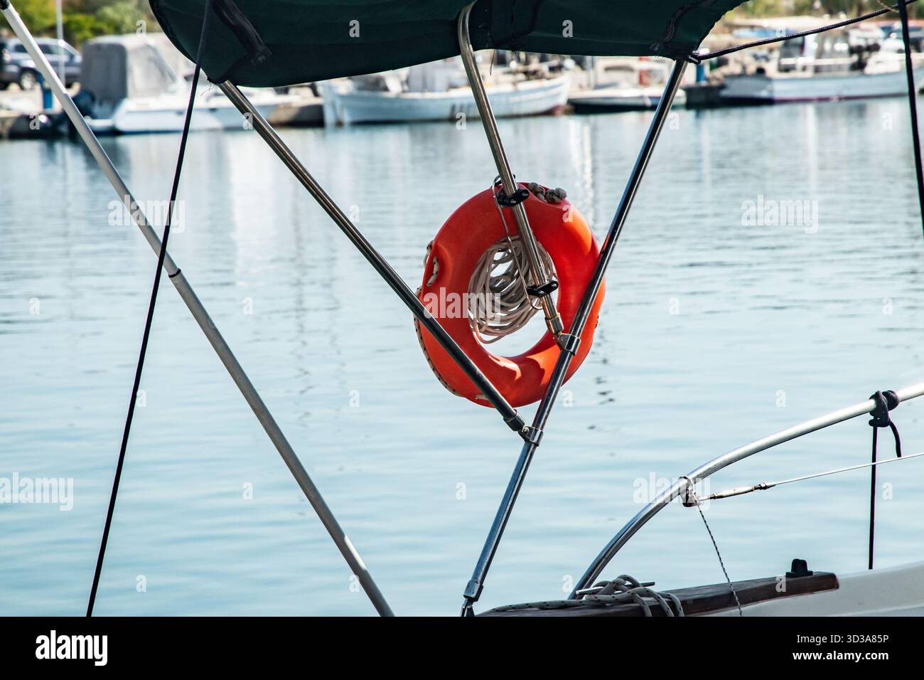 Anello di salvataggio arancione, corde e parafanghi appesi su un ringhiera per barche nel porto Foto Stock