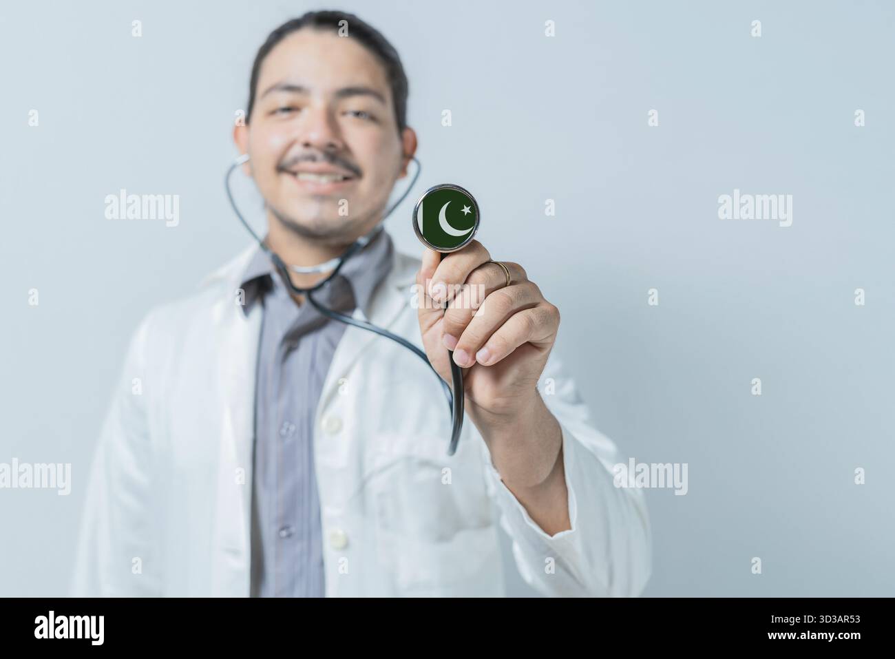 Medico sorridente mostrando stetoscopio con bandiera pakistana. Assistenza sanitaria nazionale pakistana Foto Stock