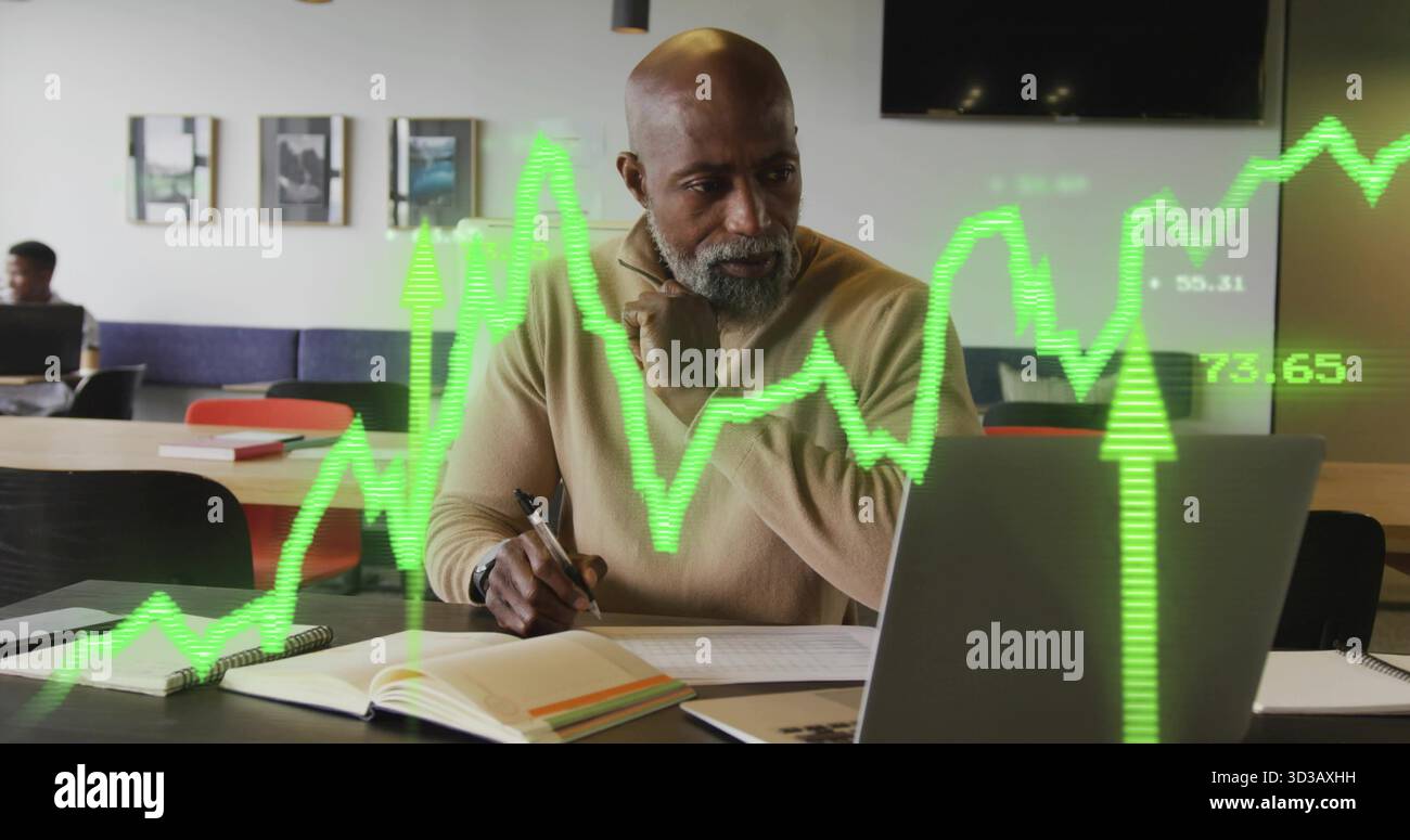 Senior Executive in maglione abbronzato con penna che rivede il laptop nello spazio di coworking, con sovrapposizione cartografica. Professionale, imprenditorialità, startup, innovati Foto Stock