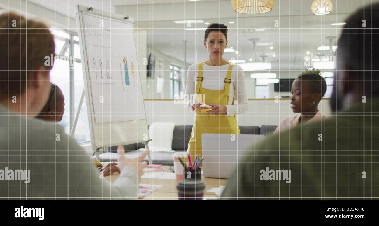 Donna in tuta gialla in piedi accanto alla lavagna a fogli mobili che presenta schizzi di design in ufficio, con pennarelli Foto Stock