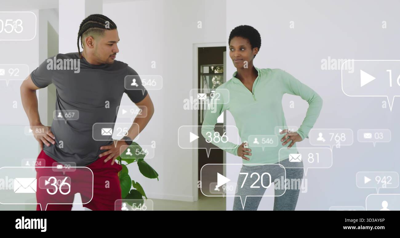 Coppia in piedi che indossa abiti da ginnastica che monitorano sovrapposizioni fluttuanti dei social media in salotto Foto Stock