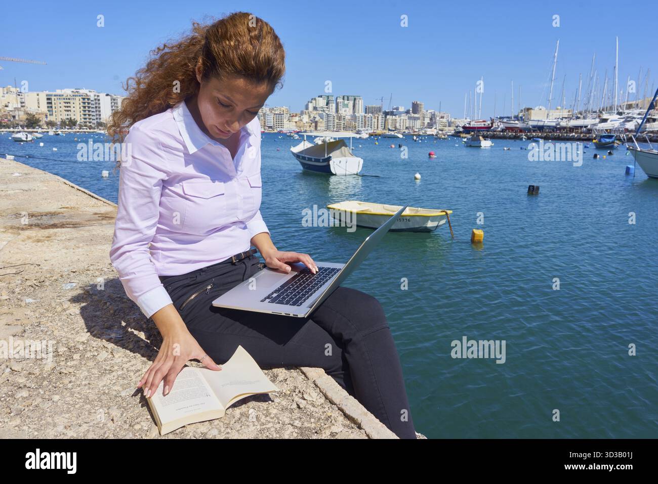 Donna che lavora con un notebook e prenota al Harbout vicino al mare nella destinazione turistica mediterranea Malta, giornalismo, giornalista, apprendimento, stude Foto Stock