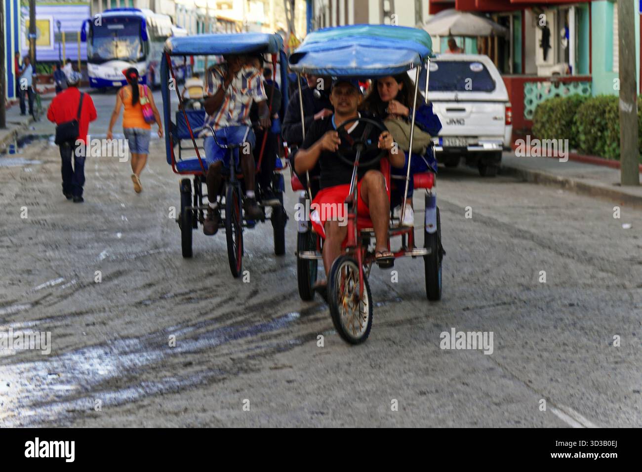Baracoa, Cuba, America centrale, taxi in bicicletta si spostano lungo una trafficata strada cittadina con persone e veicoli, Cuba, grandi Antille, Caraibi, America Foto Stock