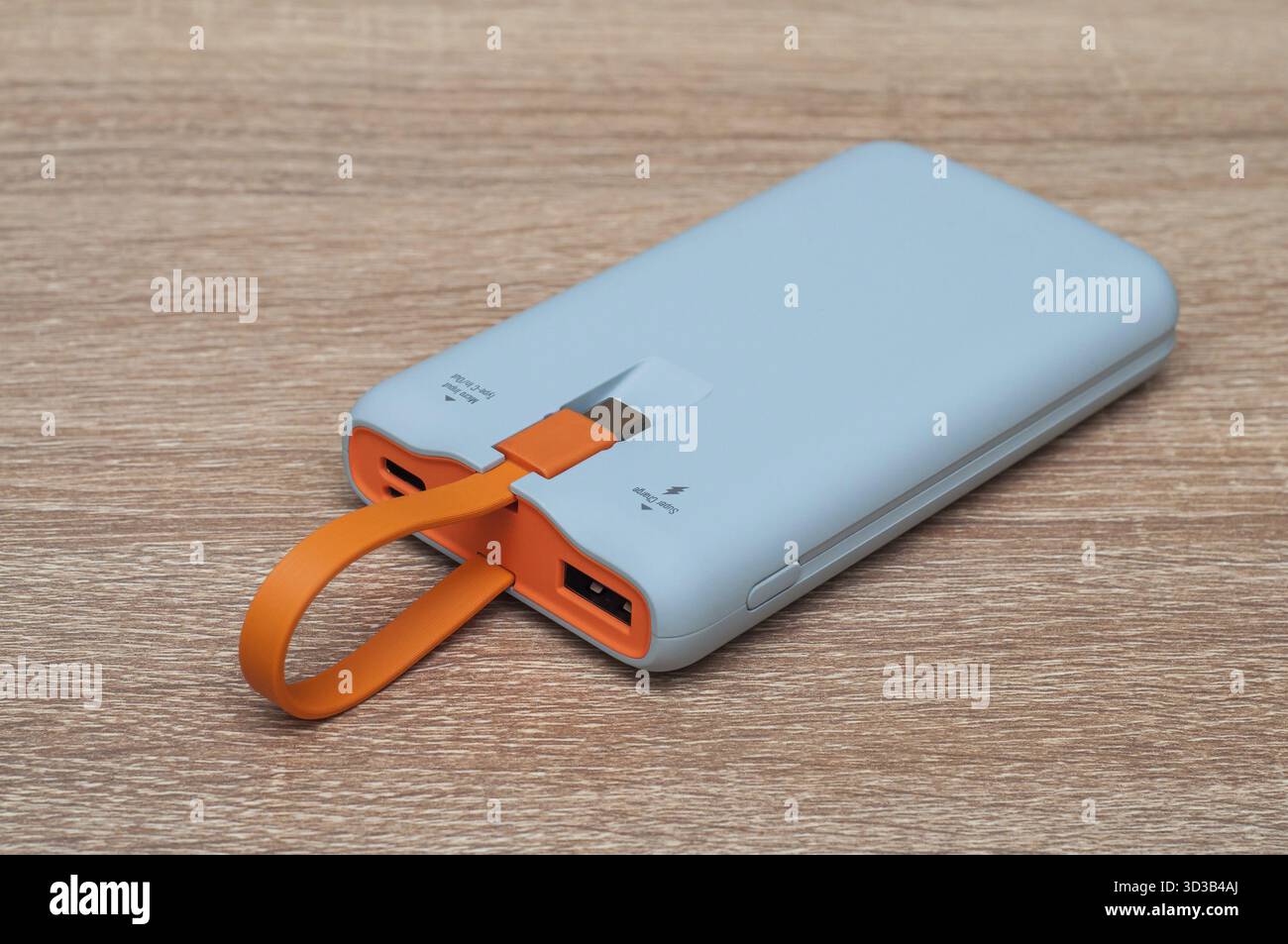 Il power Bank è grigio con una maniglia USB arancione, con connettori, pulsanti e un indicatore sul tavolo Foto Stock
