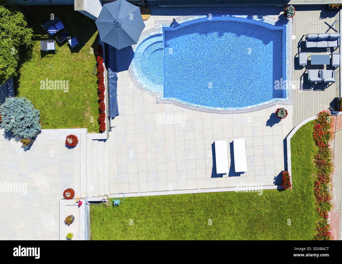 Vista dall'alto di un'elegante piscina sul cortile con design curvo, prato verde circostante e accogliente patio con posti a sedere Foto Stock