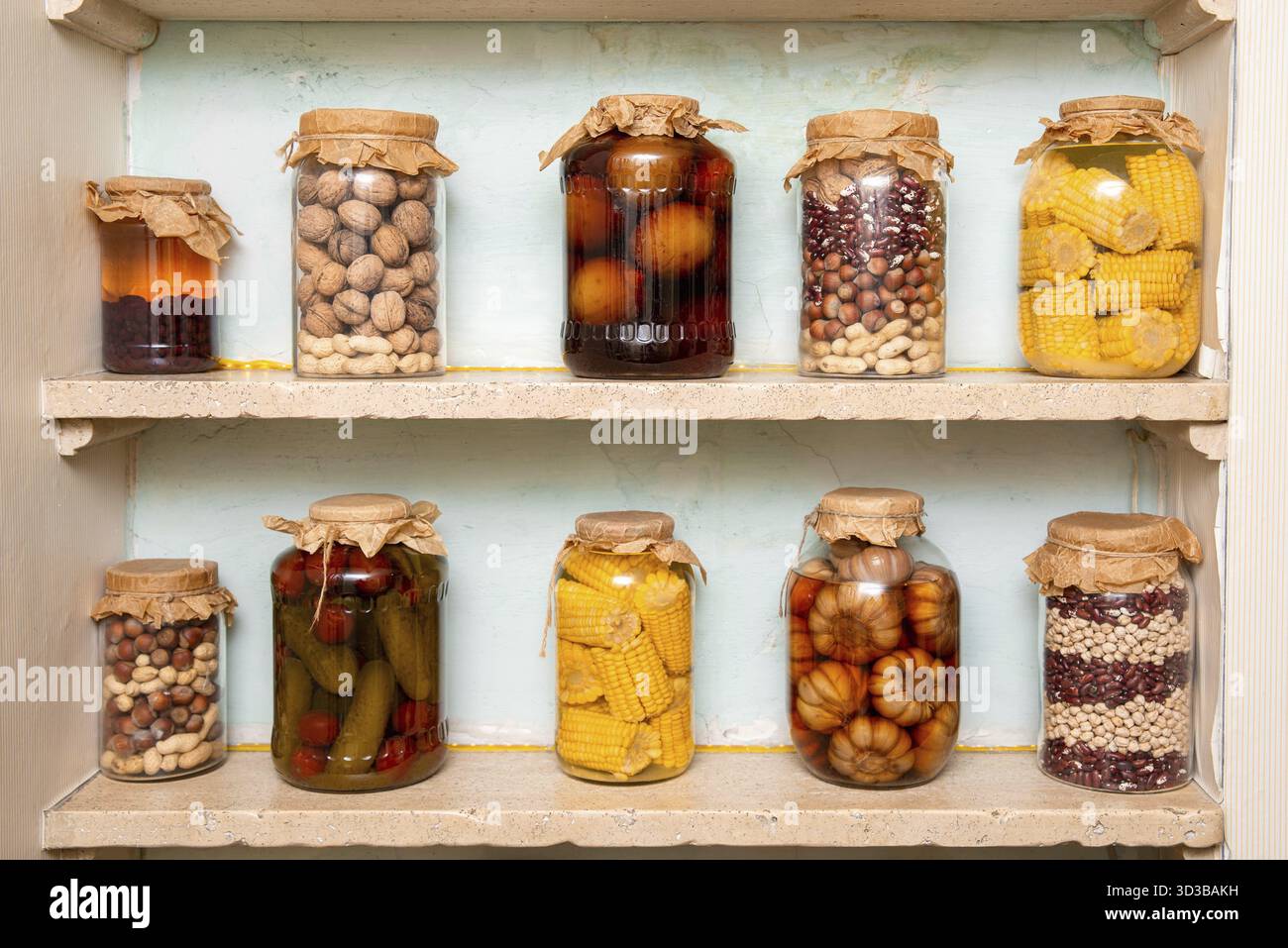 Cibo, vari cibi conservati tra cui noci, mais, fagioli e sottaceti conservati in vasetti di vetro con coperchi di carta su scaffalature rustiche Foto Stock