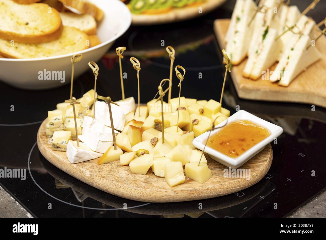 Cibo, elegante tagliere di formaggi in legno con cubetti di formaggio misti, pistacchi e un lato di marmellata, perfetto per abbinamenti di vino o antipasti Foto Stock