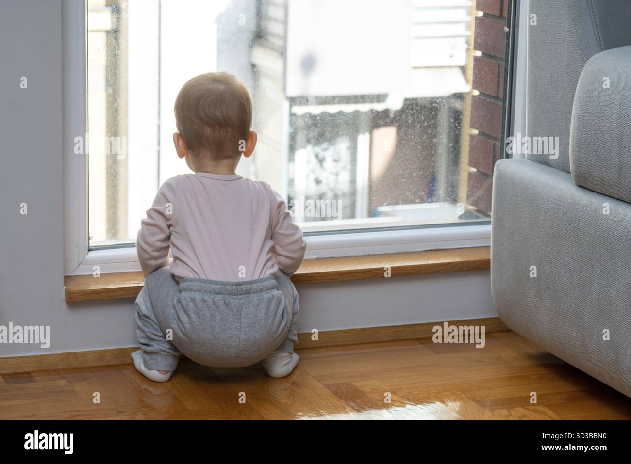 Un bambino poggia vicino a una finestra in una casa, guardando fuori con desiderio che il padre torni a casa dal lavoro. Concetto di amore duraturo e la scommessa obbligazionaria Foto Stock