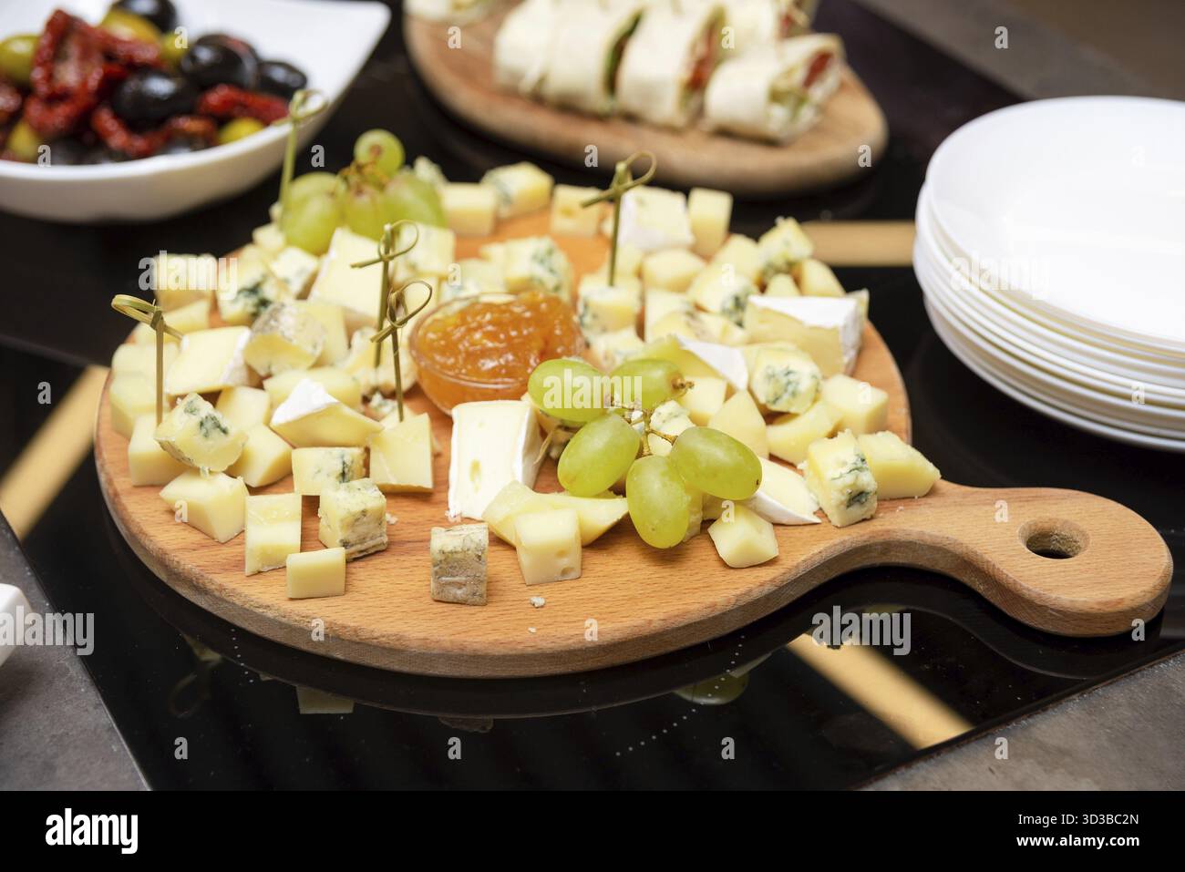 Cibo, cubetti di formaggio assortiti disposti su una tavola di legno con uva verde, spiedini e marmellata di frutta, pronti per la degustazione o l'abbinamento di vini Foto Stock