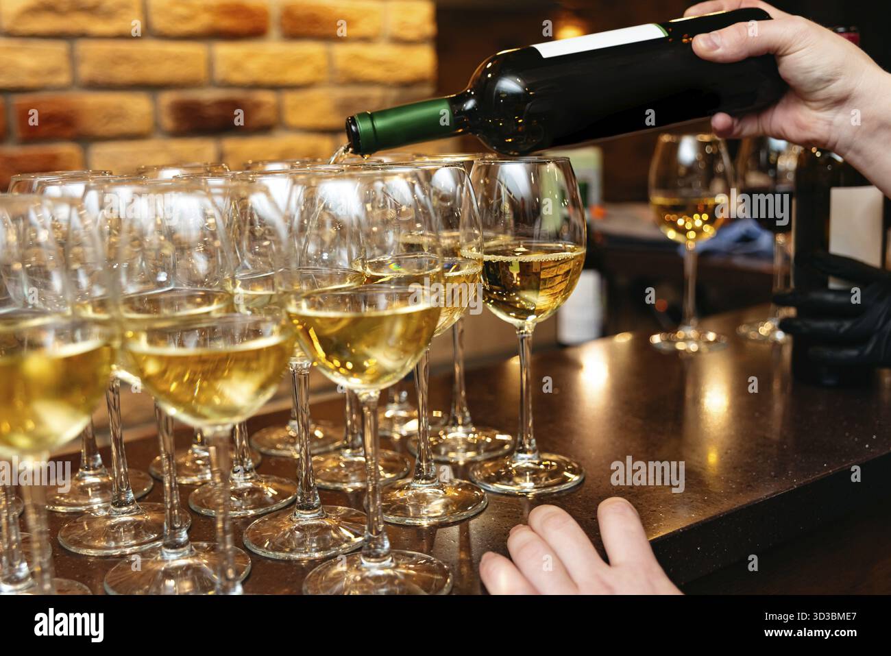 Cibo, Un barista versa vino bianco in più bicchieri presso un bar, preparandosi per un evento elegante o un'esperienza di degustazione di vini Foto Stock
