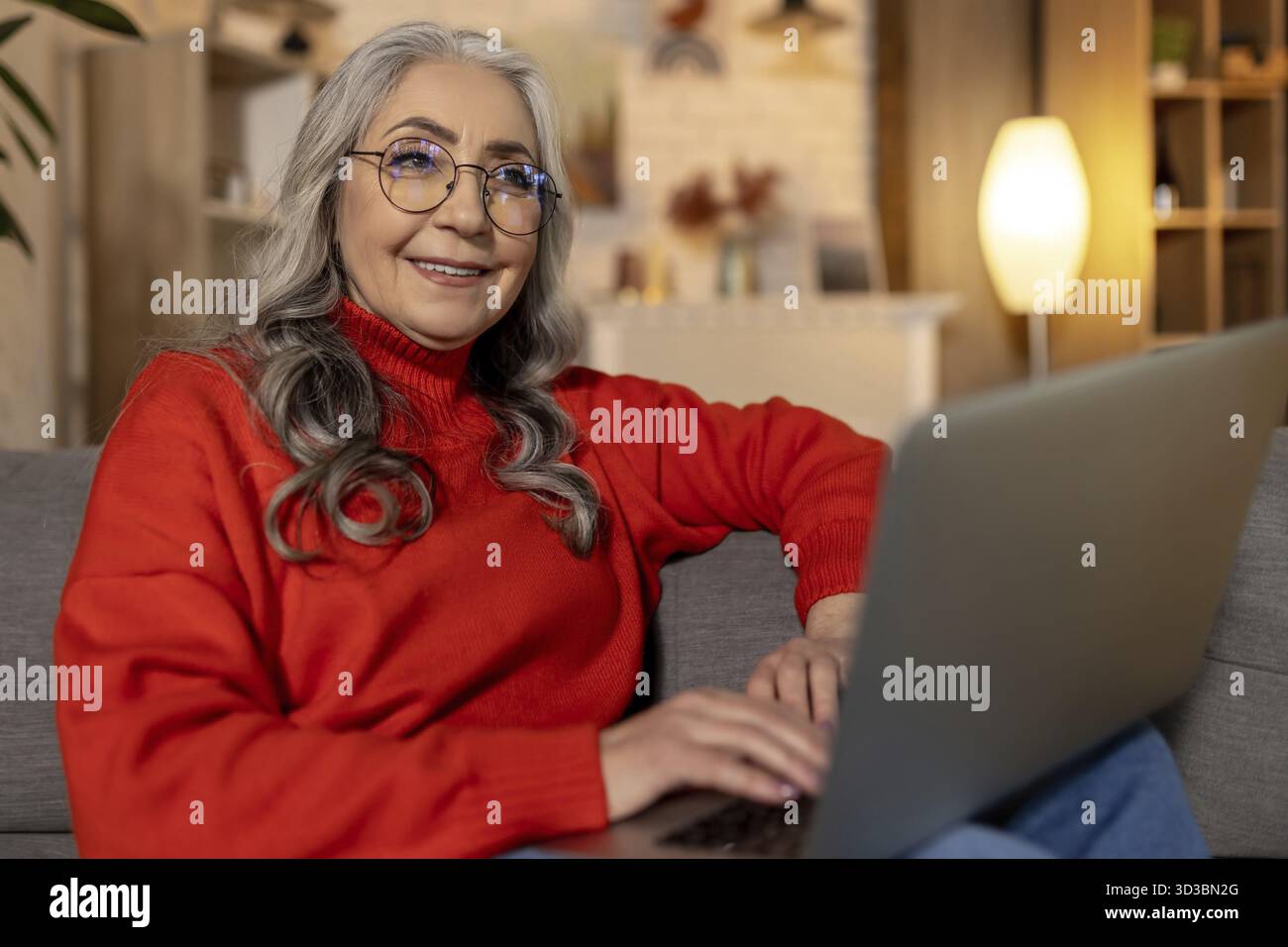 Donna a casa. Donna in camicia rossa che guarda qualcosa sul portatile Foto Stock