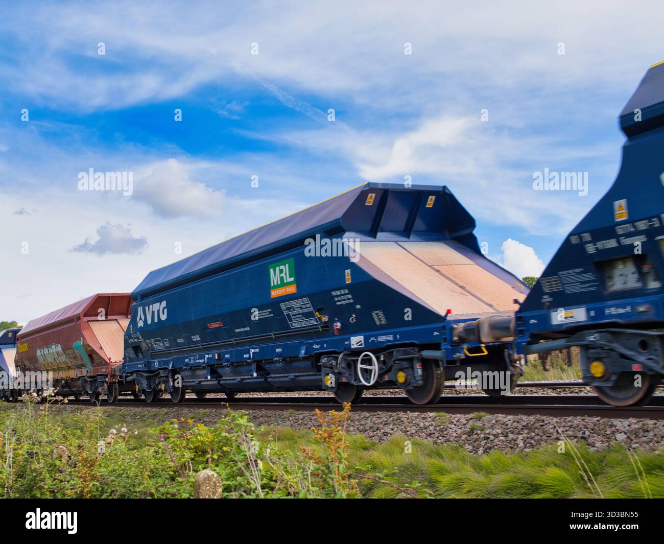 Wiltshire, Regno Unito - 09 settembre 2025: I vagoni tramoggia VTG Mendip Rail passano nel Wiltshire, nella campagna britannica sotto un cielo blu brillante, trasportando aggregati per la costruzione. Foto Stock