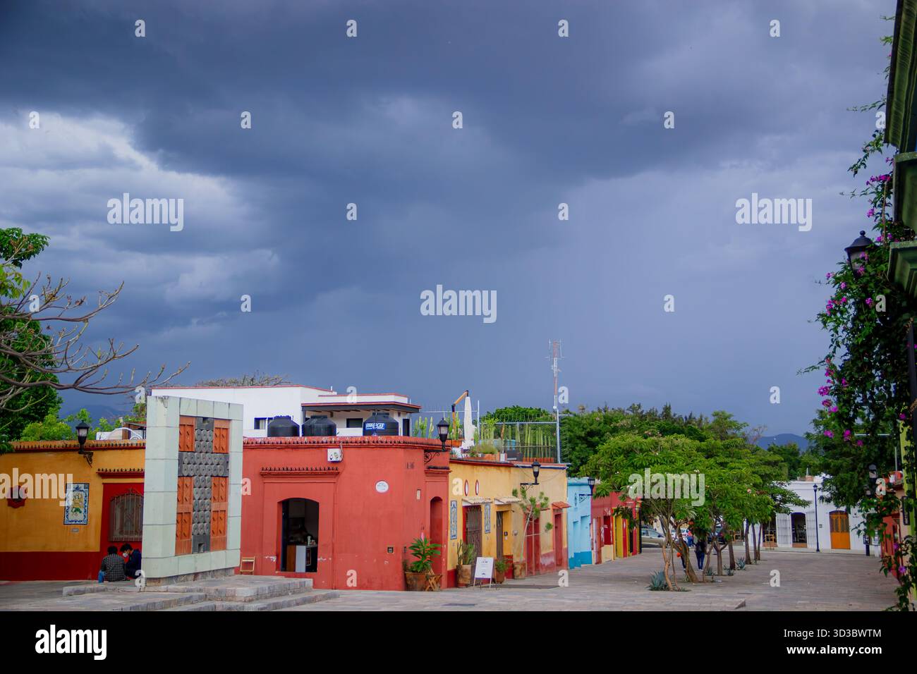 Vista prospettica di una strada con case basse dipinte di rosso e giallo, sotto un cielo buio e drammatico di tempesta in una città del Messico. Foto Stock