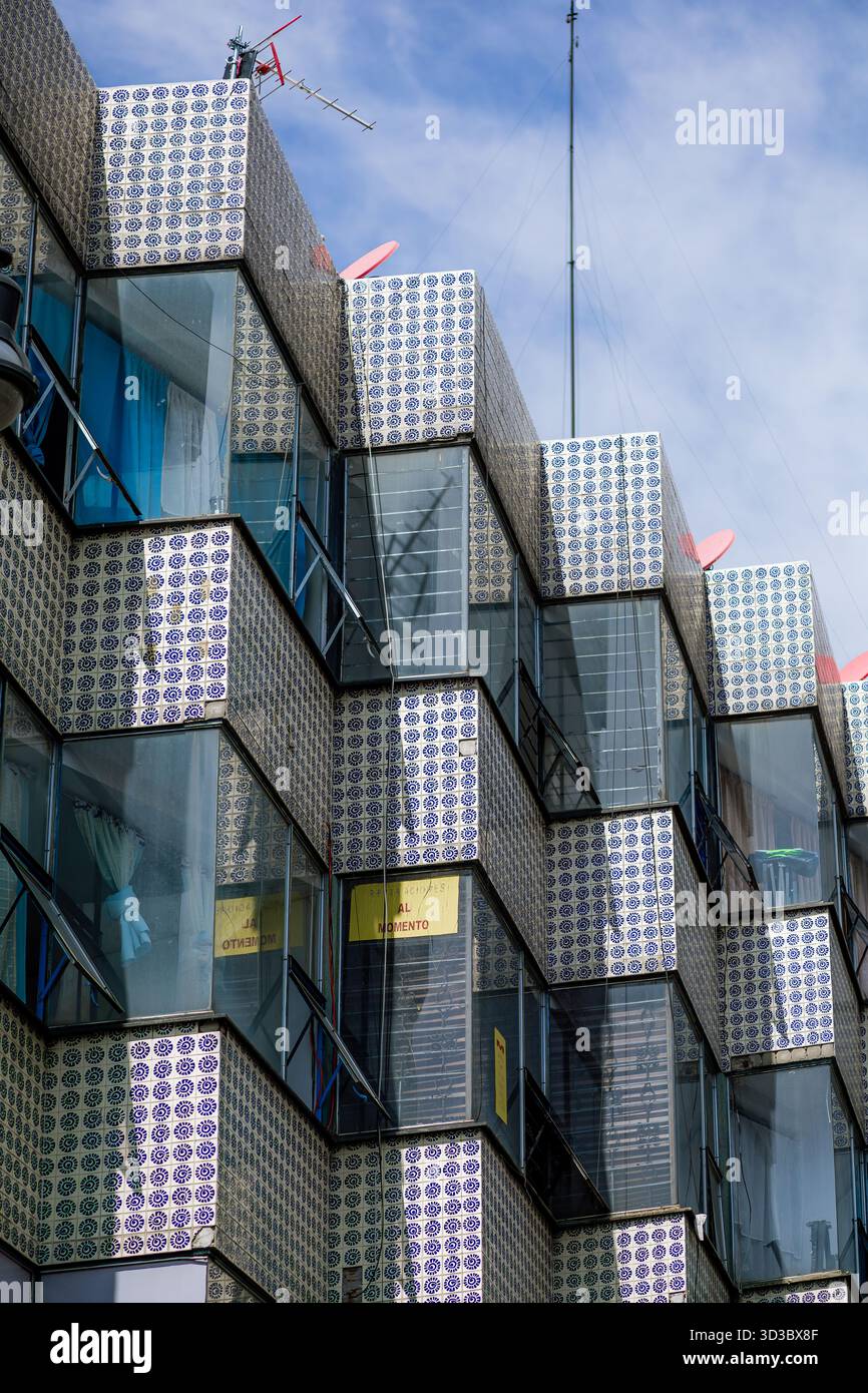 Vista ad angolo di un moderno edificio di appartamenti con finestre di vetro e una facciata rivestita in un modello ripetitivo di piastrelle viola e bianche. Foto Stock
