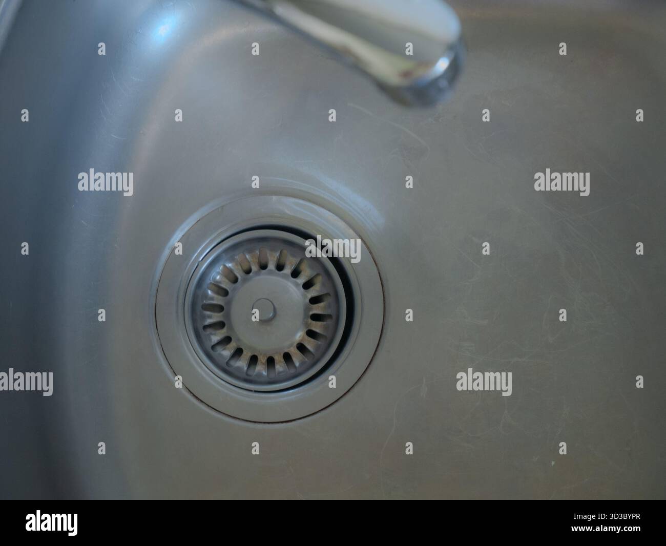 Vista ravvicinata di un lavandino da cucina pulito in acciaio inox con filtro a rete e rubinetto in metallo, che mostra un design moderno minimalista e una superficie liscia Foto Stock