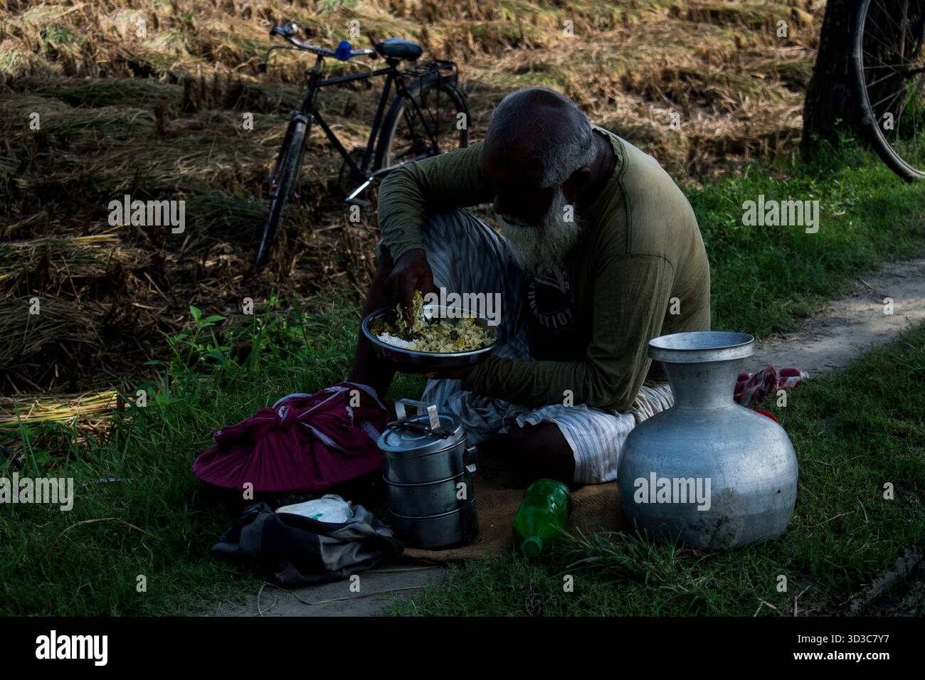 il vecchio contadino del villaggio sta pranzando accanto alla terra agricola. Foto Stock