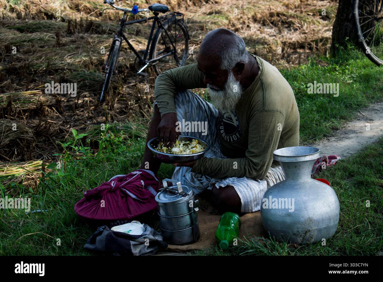 il vecchio contadino del villaggio sta pranzando accanto alla terra agricola. Foto Stock