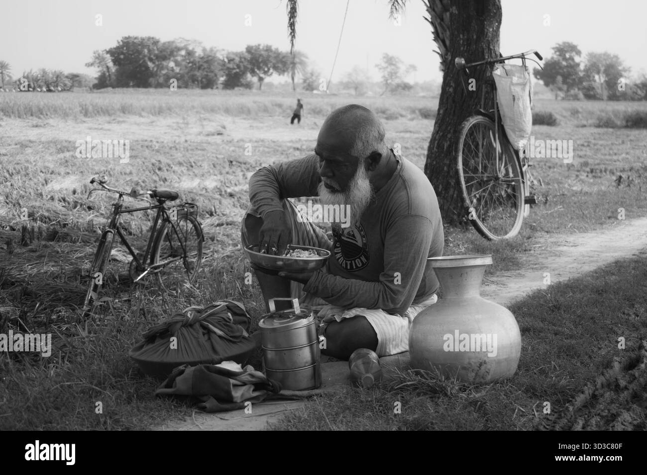 il vecchio contadino del villaggio sta pranzando accanto alla terra agricola. Foto Stock