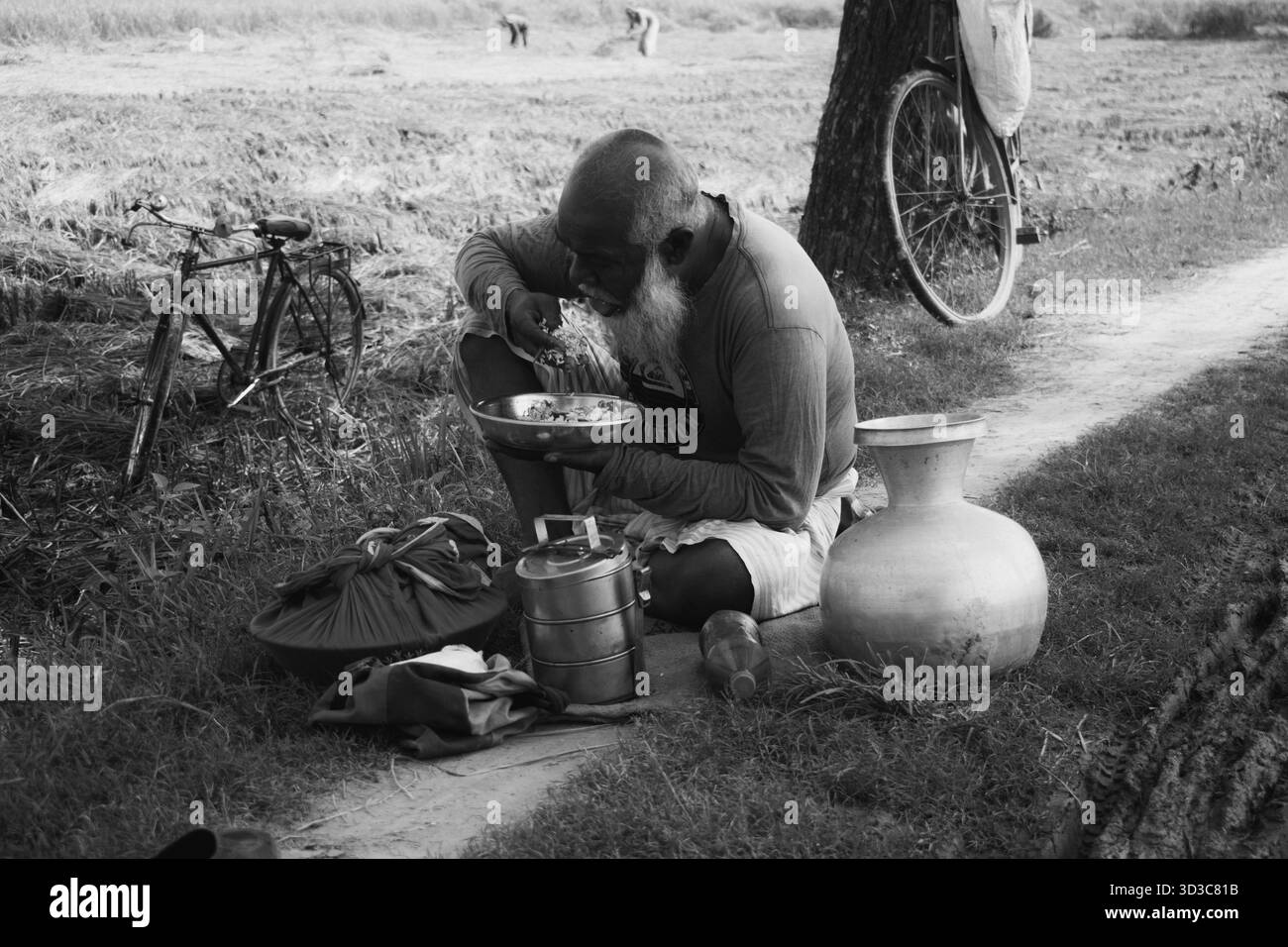 il vecchio contadino del villaggio sta pranzando accanto alla terra agricola. Foto Stock