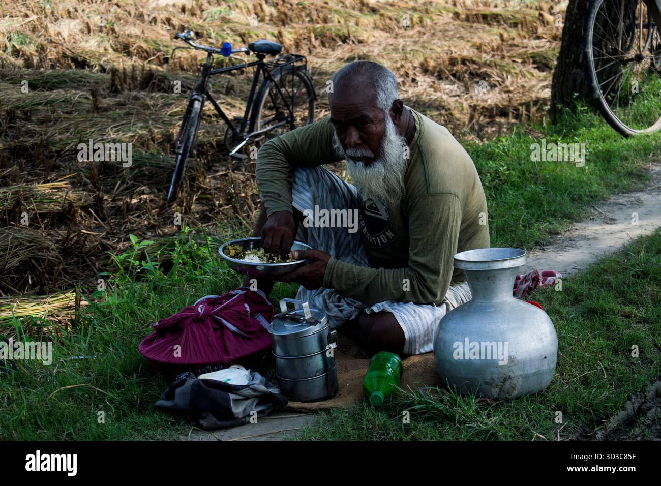 il vecchio contadino del villaggio sta pranzando accanto alla terra agricola. Foto Stock