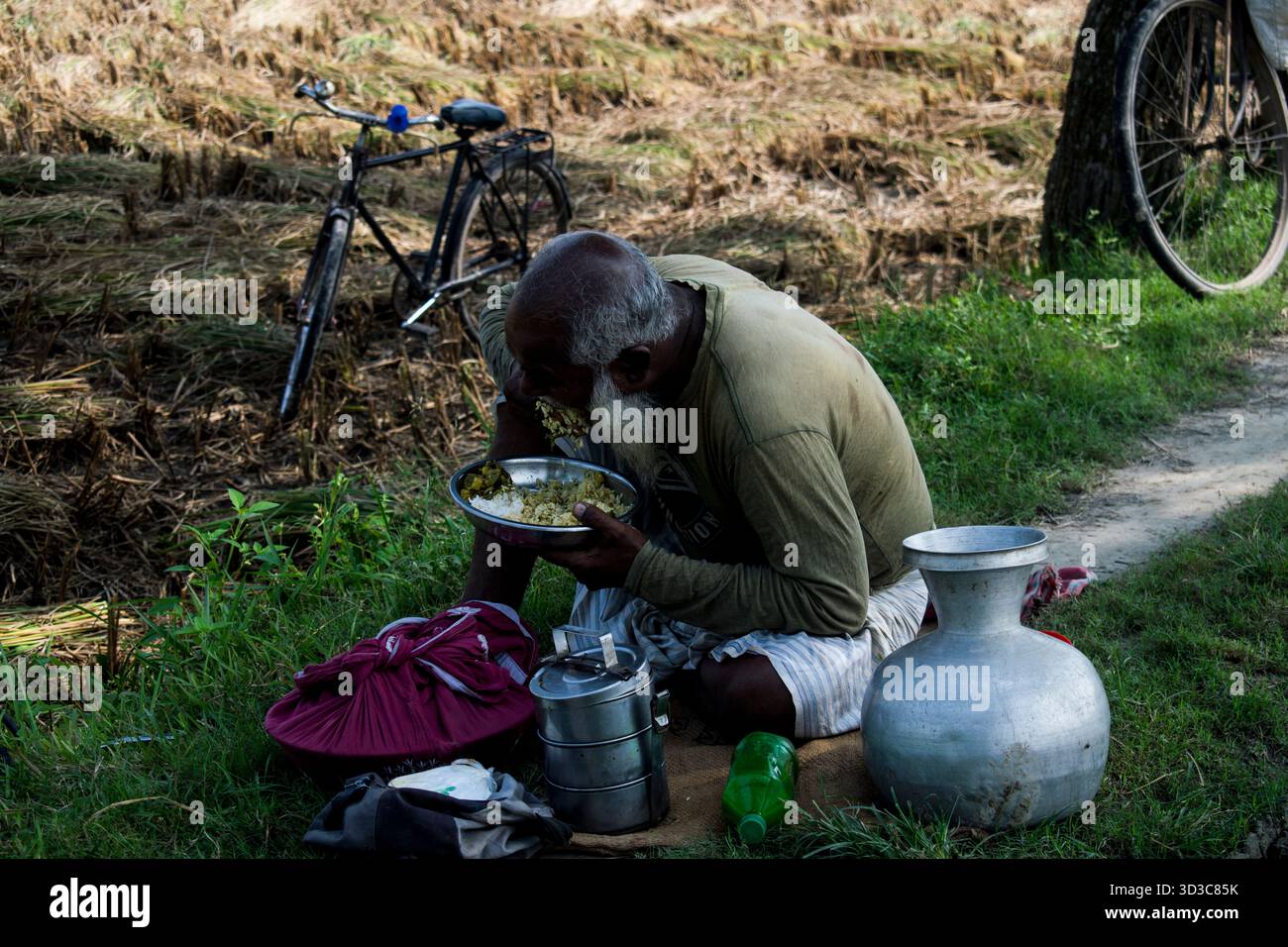 il vecchio contadino del villaggio sta pranzando accanto alla terra agricola. Foto Stock
