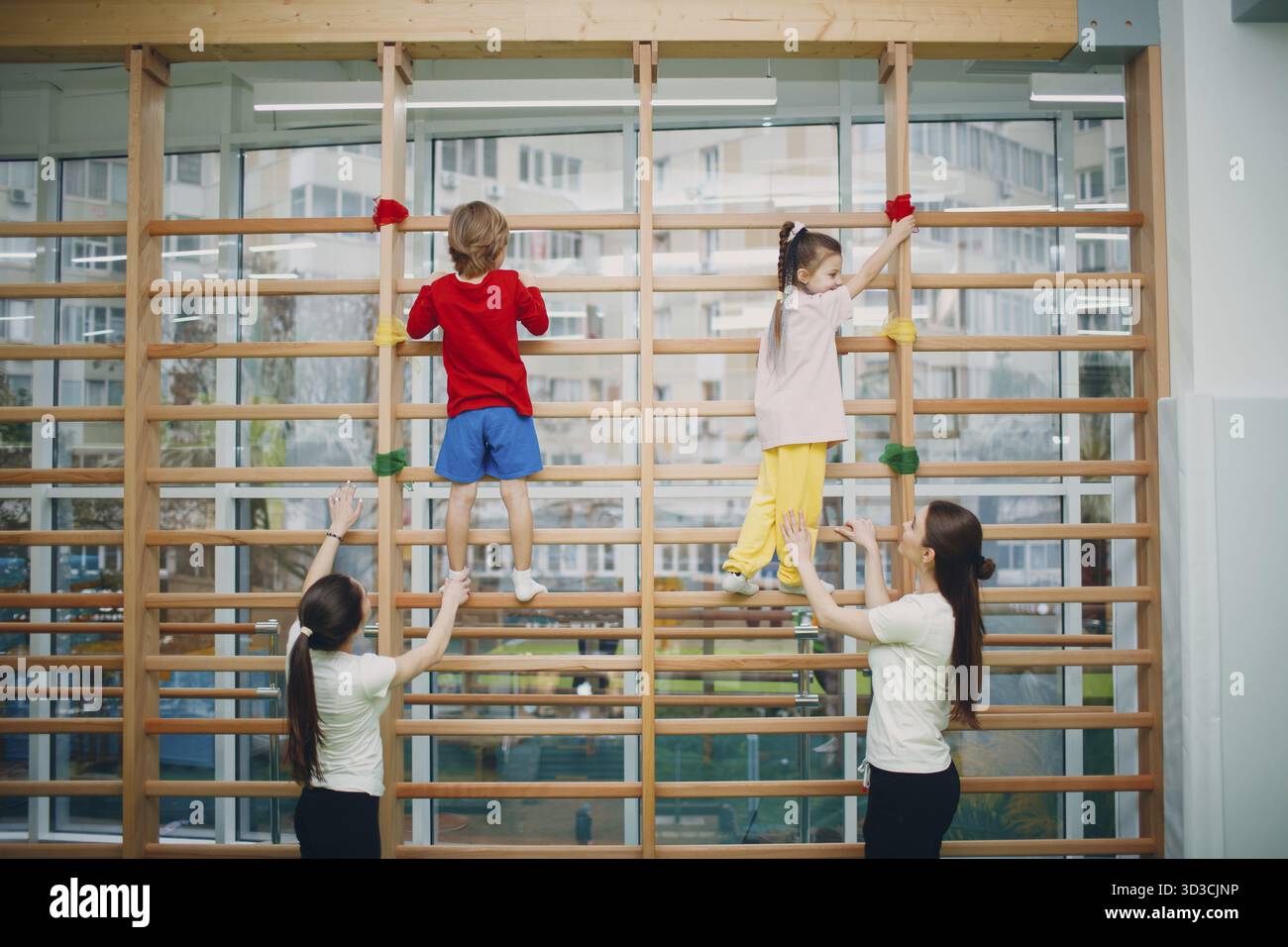 Bambini alle pareti svedesi esercizi in palestra presso l'asilo o scuola elementare con insegnanti. Concetto di sport e fitness per bambini Foto Stock