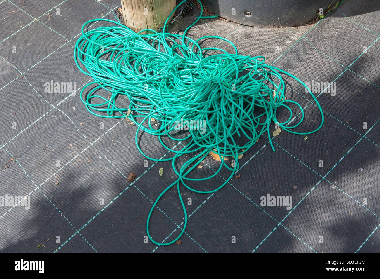 Tubo flessibile per legare il giardino visualizzato sulla membrana per erbacce. Concetto di fornitura di giardinaggio Foto Stock