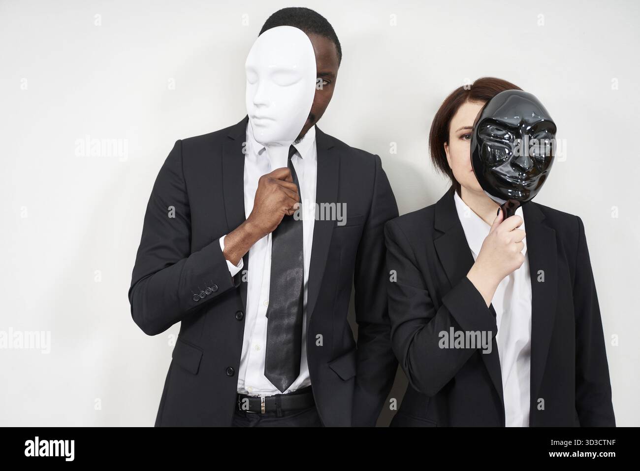 Uomo africano e donna caucasica che indossa abiti neri che nascondono il viso con le maschere Foto Stock