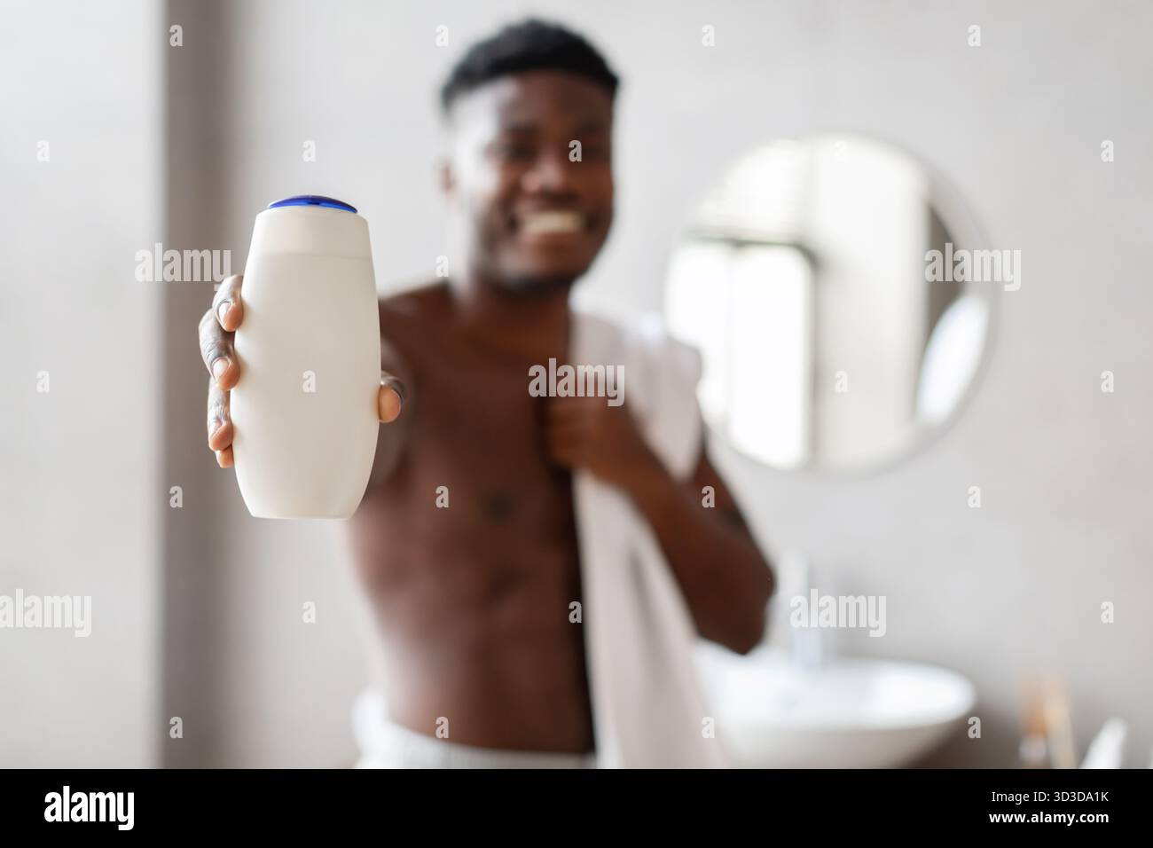 Uomo nero che promuove il prodotto per la cura del corpo in bagno mentre è avvolto in un asciugamano Foto Stock