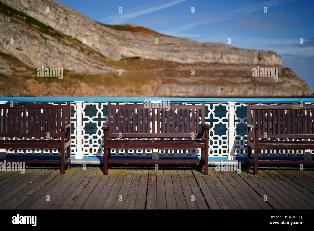 panche in legno su un molo con una collina rocciosa sullo sfondo Foto Stock
