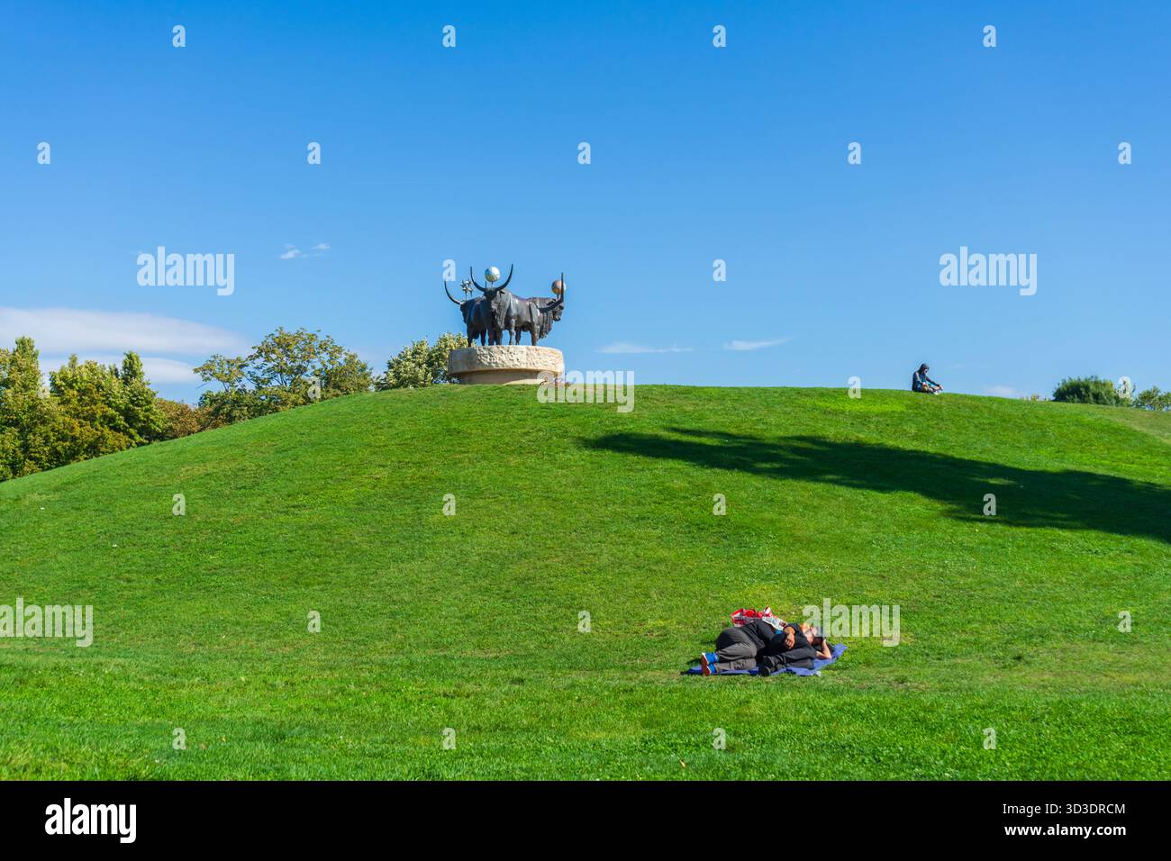 Riposati sulla collina illuminata dal sole del parco Bikás sotto la statua del toro "Monda" di Kiss István, simbolo del rinnovamento urbano verde di Újbuda. Foto Stock